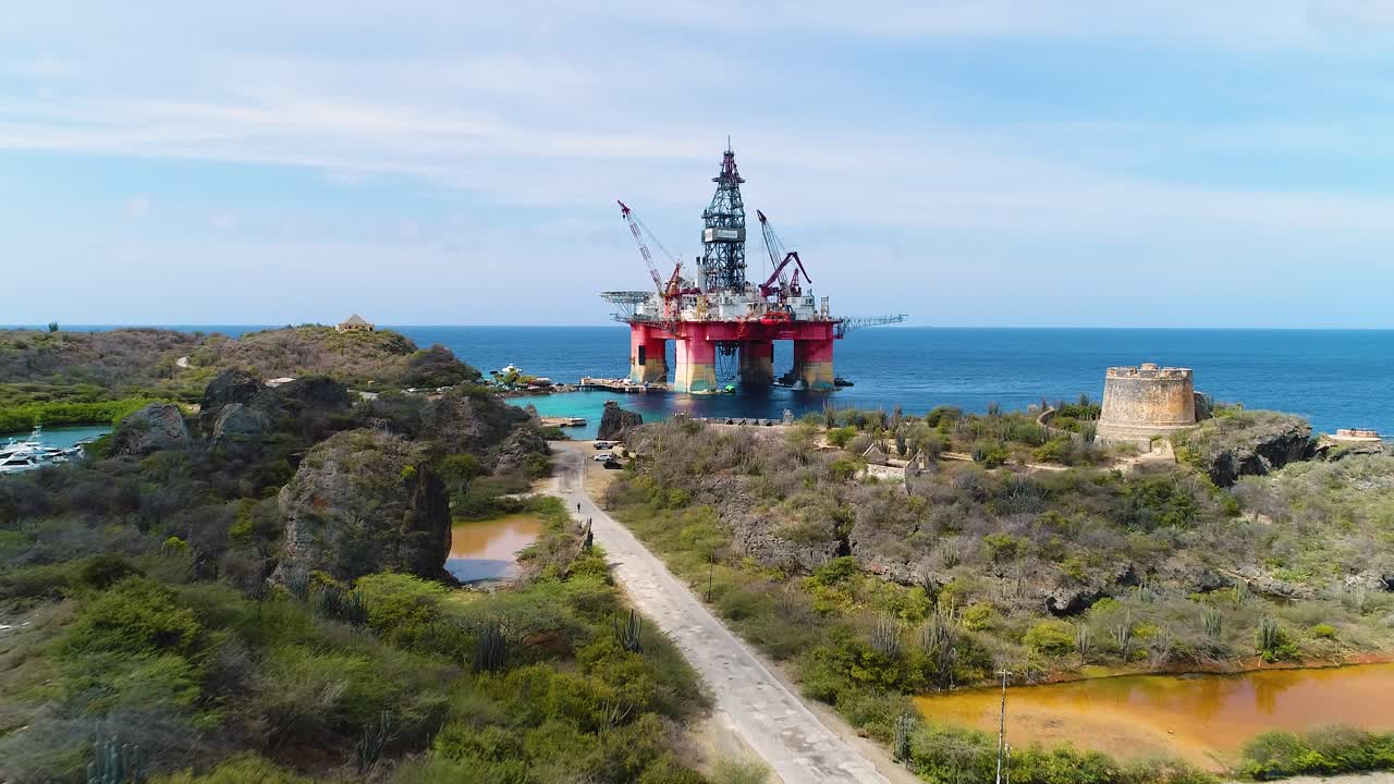 Gammel forladt offshore-olieboreplatform i Caribiens kystfarvand ved en tør kystørken.