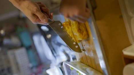 Kitchen-knife-used-to-cut-egg-omelet-on-wooden-kitchen-cutting-board,-filmed-in-vertical-closeup-handheld-slow-motion-shot