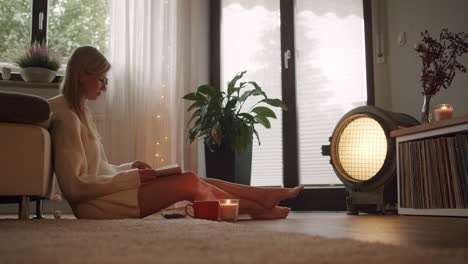 young blonde woman reading a book on the floor in the living room, wide angle, cozy