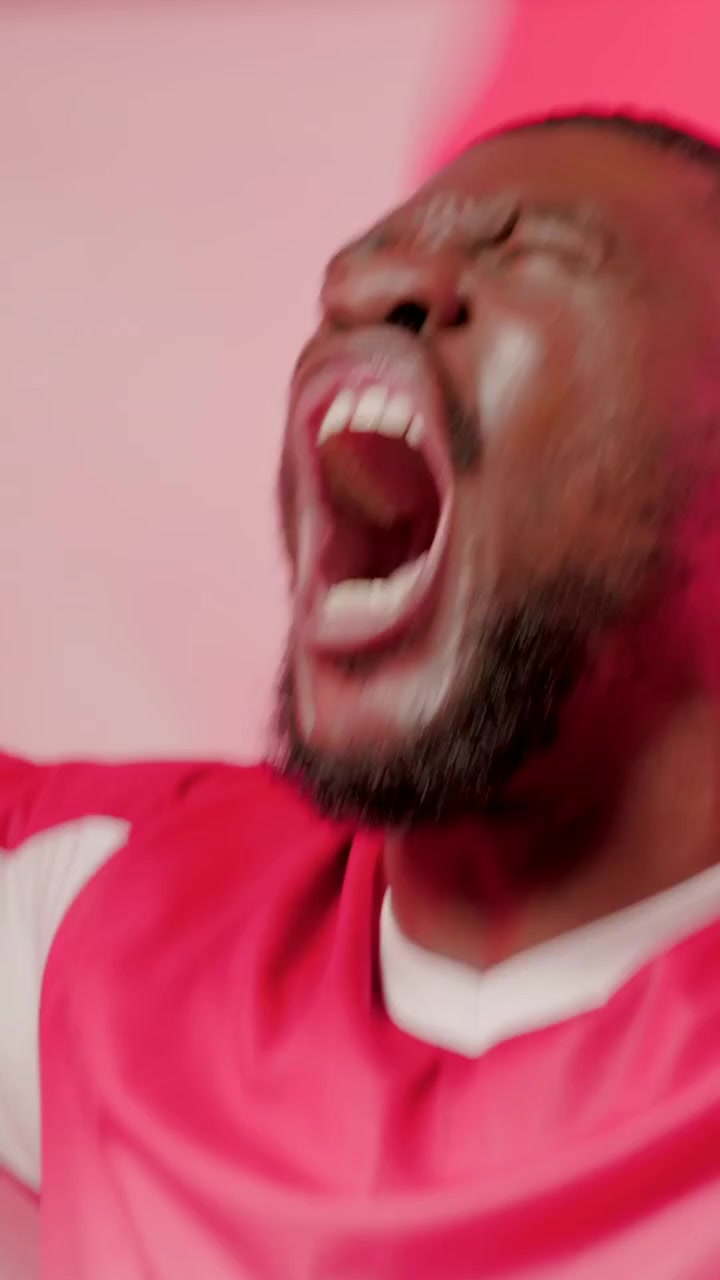 Vídeo vertical: Após o gol, homem de boné vermelho e camisa gritando e acenando bandeira no quarto, celebrando