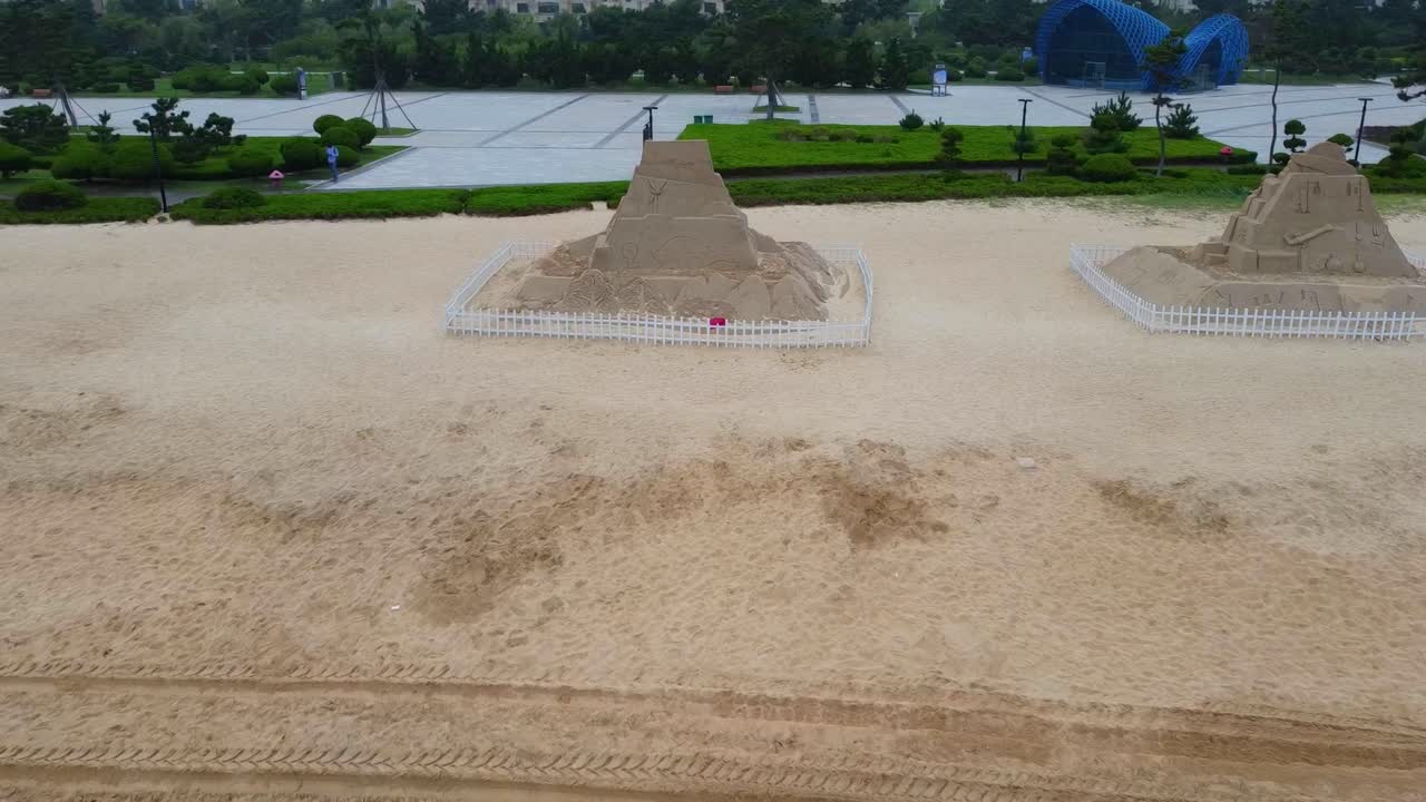 Beach sand pyramids with different themes etched on sand sculptures with green natural garden background