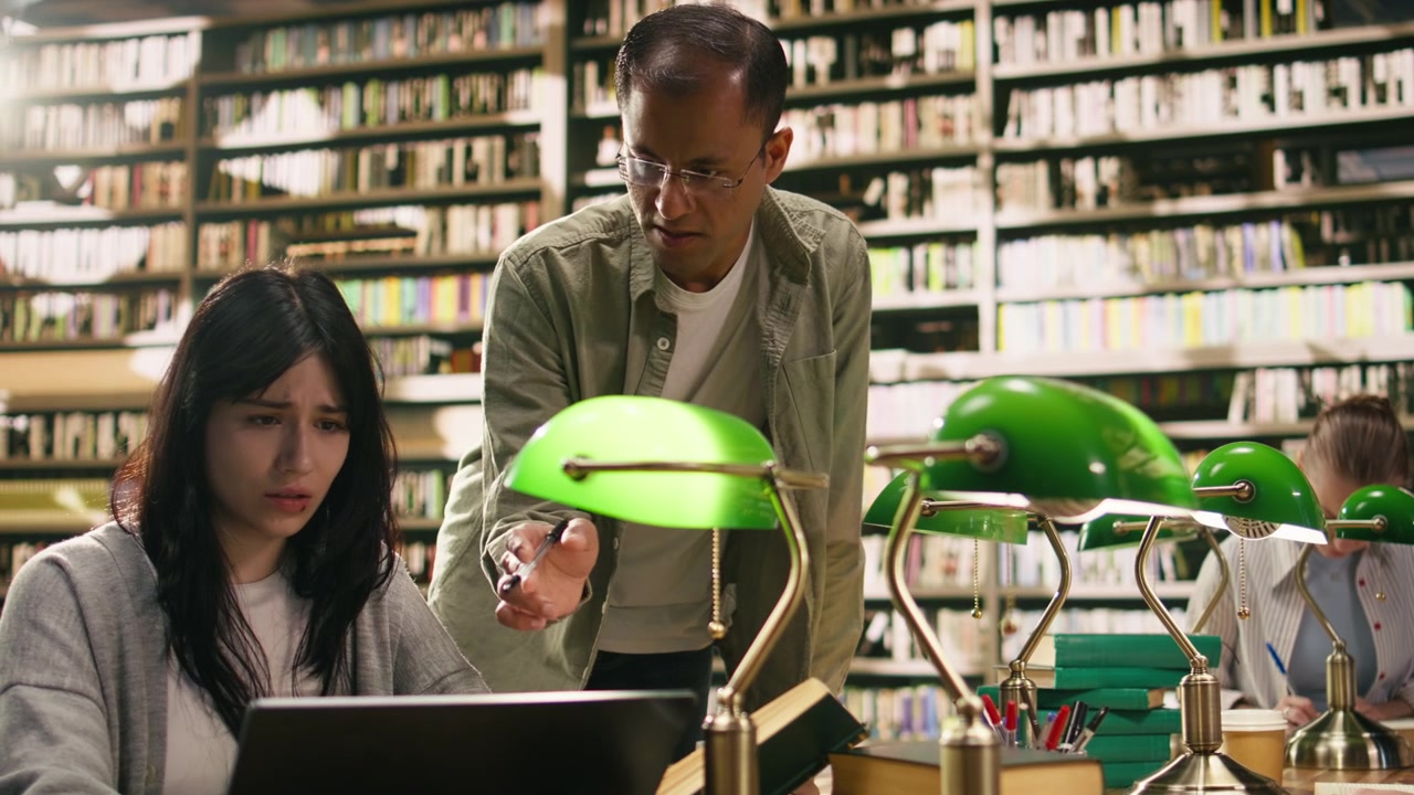 Tutor leaning over explaining coursework to student on laptop