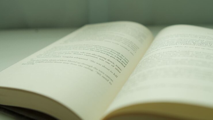 Primo piano di un dito che sfoglia una pagina di un libro da sinistra a destra, su una scrivania vicino alla finestra di casa.
