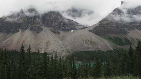 dramatic slopes descend from mist-shrouded peaks, with dense forest and a hint of a turquoise lake