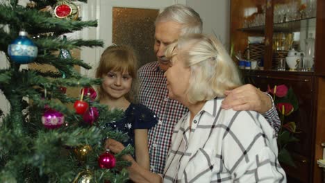 niña linda con abuelos mayores familia decorando árbol de navidad artificial en casa
