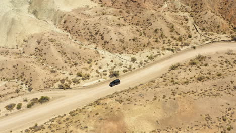 dark black suv drives slowly down a dirt road passed a dirt pullout in the middle of a dry and desolate desert