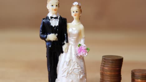 miniature bridal couple standing beside stack of coins