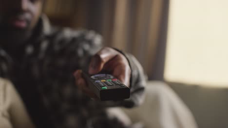 close up of man relaxing at home sitting on sofa changing tv channels with remote control