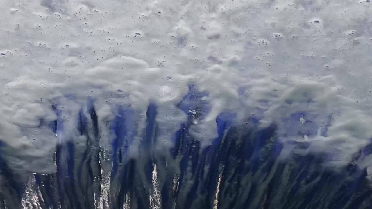 автоматическая проходная автомойка, как видно через переднее стекло автомобиля, создающая узоры, стекающие по стеклу