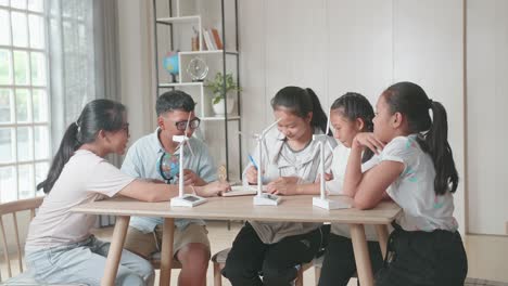 asian group of thoughtful kids study about ecology problems and their solution with wind turbine model and globe at school. renewable energy