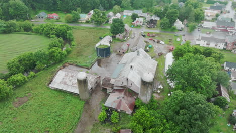 aerial orbit: old farm with grain silos and rusted metal roofs adjacent to open field