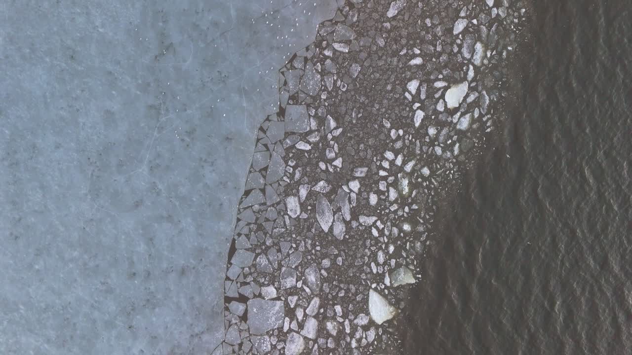 top down drone shot of a frozen body of water transitioning from solid ice, to broken ice, to water