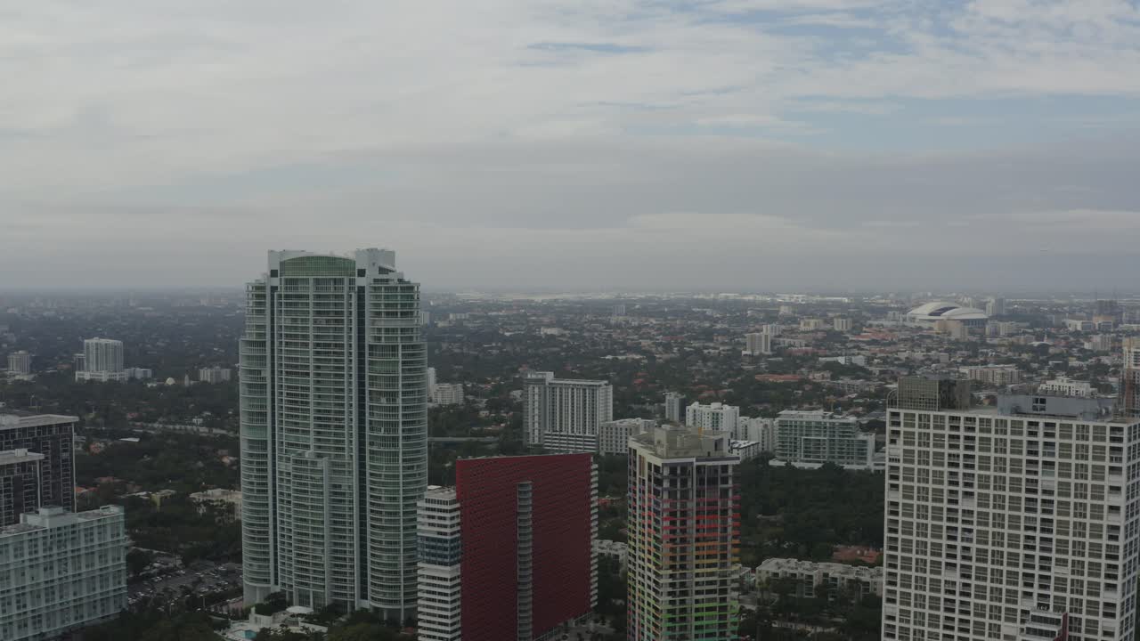 Vista aérea se movendo em direção a alguns edifícios no centro de Miami, com as áreas urbanas de Miami ao fundo
