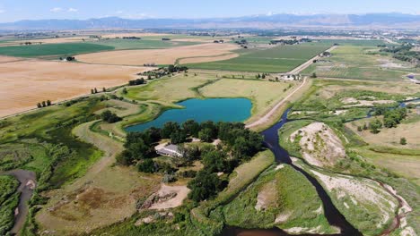 Panoramic-video-of-a-rural-landscape-with-a-stunning-blue-lake-along-pasturelands-each-side,-and-abundant-greens-on-the-other,-and-distant-mountains-over-the-horizon,-in-Colorado