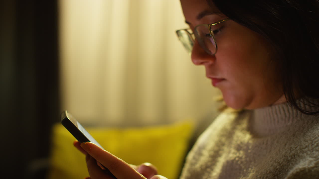 primer plano de una mujer joven pasando la noche en casa sentada en el sofá con el teléfono móvil desplazándose por internet o las redes sociales 1