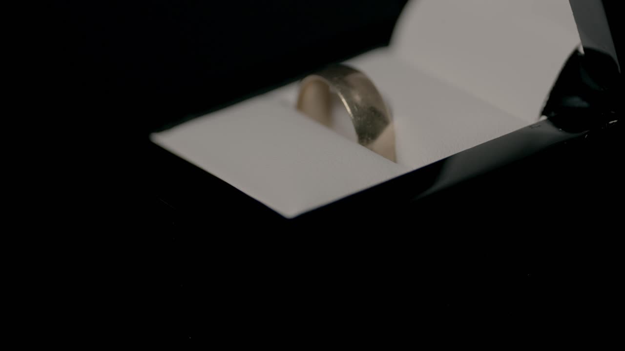 Detailed view of a polished silver ring nestled within an elegant open box. The dim lighting highlights the ring's shiny surface, creating a sophisticated and luxurious mood