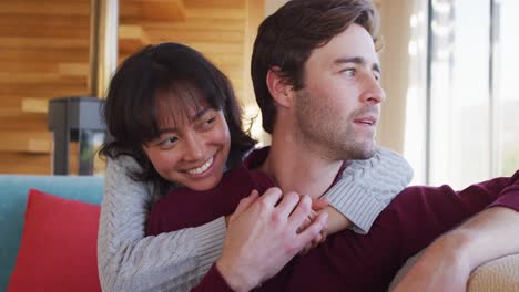 Video-of-back-view-of-happy-diverse-couple-sitting-on-sofa-and-embracing