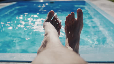 un hombre se está relajando junto a su piscina, las piernas son visibles en el marco