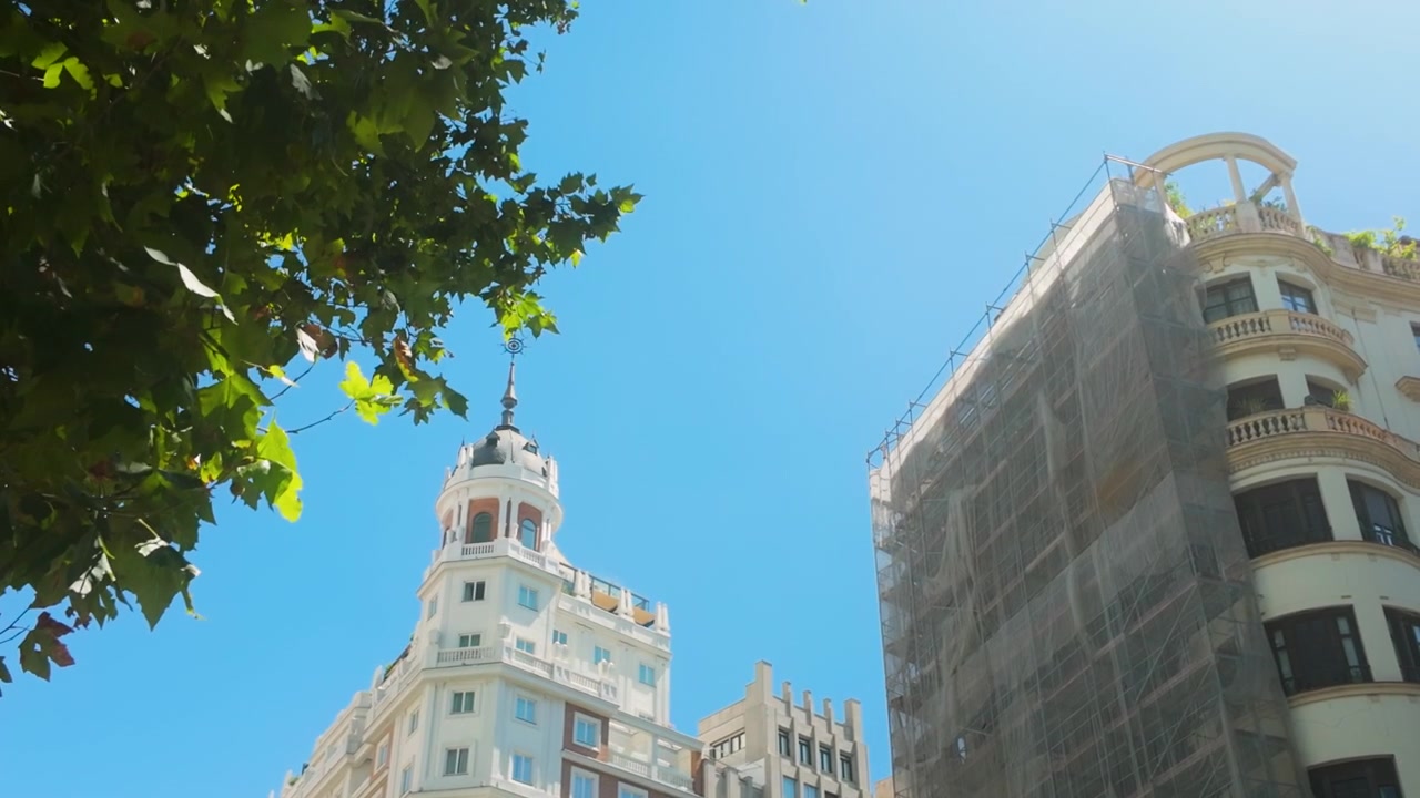 Uma Vista de Baixo Ângulo de Edifícios Brancos Ornamentados e uma Torre com Cúpula em Madrid, Espanha, Emoldurada por Folhas de Árvores Verdes Contra um Céu de Verão Claro