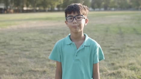 portrait of cute latin boy standing in park and smiling at the camera