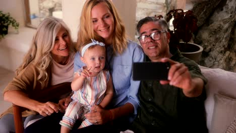 senior couple with daughter and granddaughter taking selfies at home