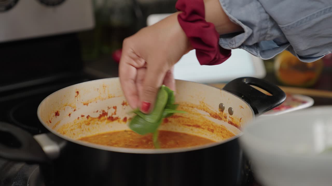 la mano de una mujer joven colocando hojas de espinacas en un curry de garbanzos dorados calientes