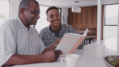 young black man looking at a photo album at home with his grandfather, close up