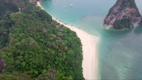 splendid aerial shot over a beautiful mountainous tropical island with several boats on the shoreline below