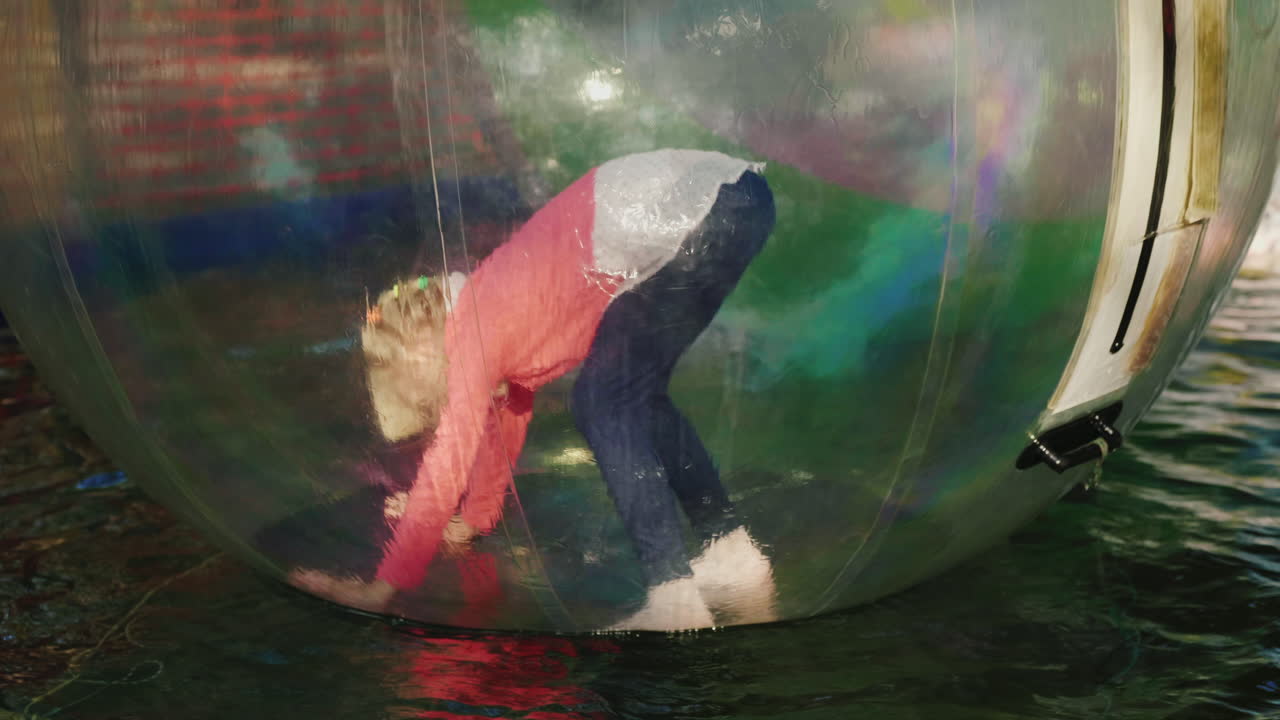 la niña intenta hundirse sobre sus pies y mantener el equilibrio dentro de la bola transparente que flota en t