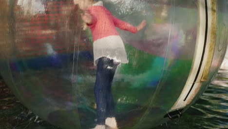 the girl tries to sink on her feet and keep the balance inside the transparent ball that floats on t