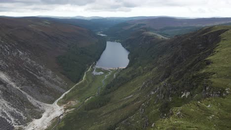 Overflying-The-Lush-Green-Forest-And-Mountain-Range-In-Glendalough-Overlooking-The-Upper-Lake-At-Daytime-In-Wicklow,-Ireland