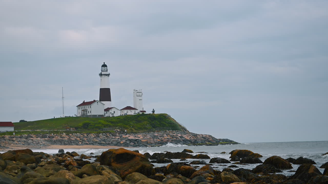 Montauk Lighthouse, New York, USA on a gloomy dull day. Waves splash by the rocks at the waterfront