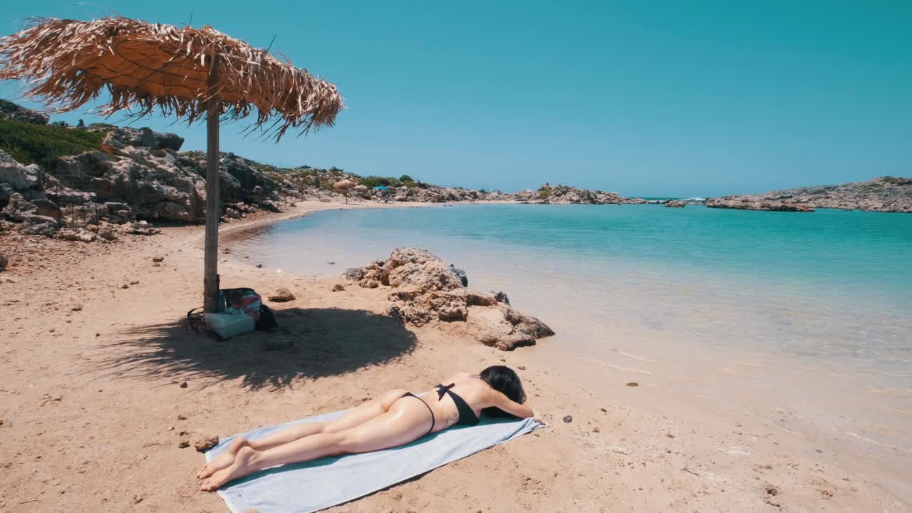 Woman laying on a towel on beach under the sun in Crete, Greece