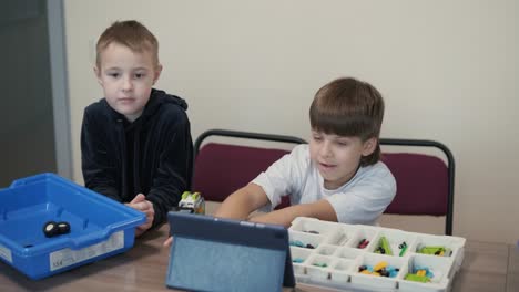 children intently focused on assembling parts from a robotics kit, with a tablet displaying instructions, promoting stem learning and creativity