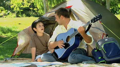 Padre-Tocando-La-Guitarra-Para-Su-Hijo-Frente-A-Una-Tienda-De-Campaña