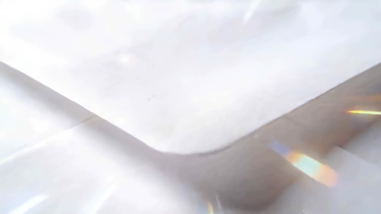 Moving camera examining white envelope V-flap on reflective table, showing sheet beneath and flares