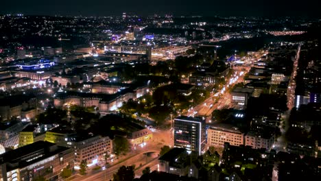 Aerial-night-time-lapse-in-4k-of-downtown-city-skyline-in-Stuttgart,-Germany-spinning-and-panning-down