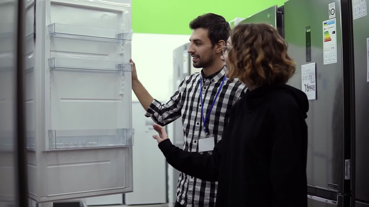 mujer joven de pie abriendo la puerta del refrigerador con un consultor masculino discutiendo el diseño y la calidad antes de comprar en un consumidor