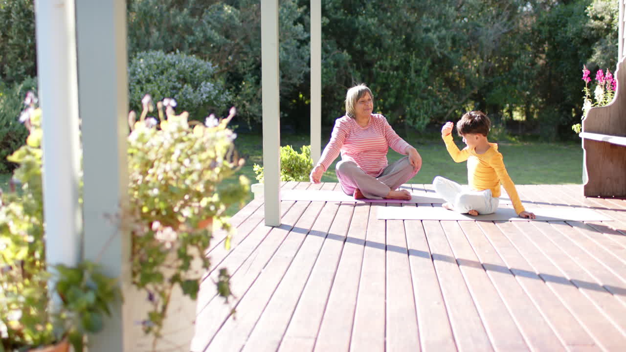 Glad ældre biracial bedstemor og barnebarn, der laver yoga og strækøvelser, slow motion, med plads til tekst