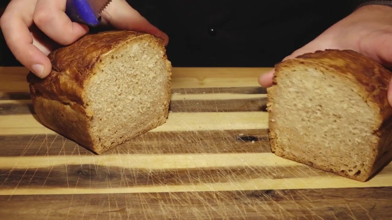 A person uses a serrated knife to slice loaves of fresh homemade bread on a rustic wooden cutting board.