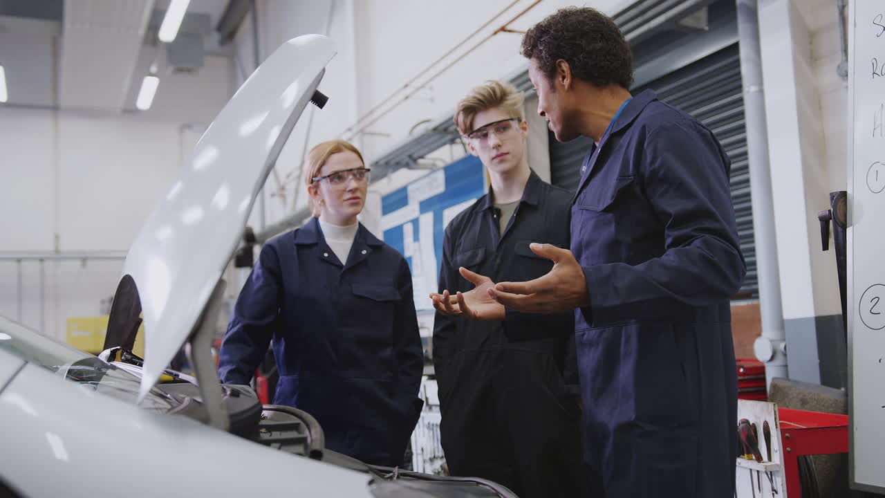 tutor masculino con estudiantes mirando el motor del coche en el curso de aprendizaje de mecánico de automóviles en la universidad