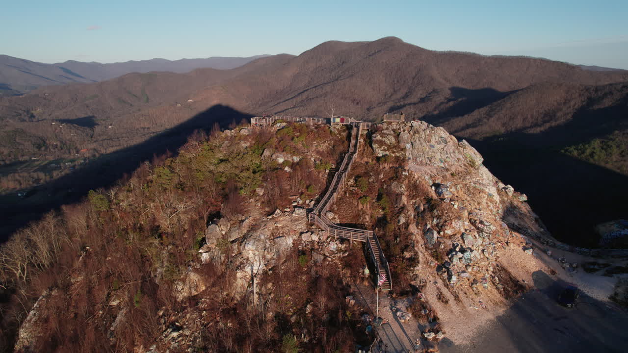 A wide drone shot of Bell Knob lookout at sunset revealing the peak of the old quarry and popular tourist hiking location for beautiful views of the north Georgia mountains near Hiawassee.