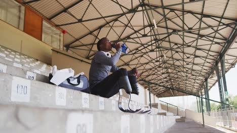 disabled mixed race man with prosthetic legs drinking water and looking away