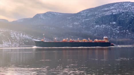 a cargo ship sailing down the hudson river in winter in new york state in the hudson valley during winter with snow in the mountains and ice in the water