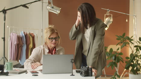 Senior-Businesswoman-Using-Laptop-and-Talking-with-Young-Colleague