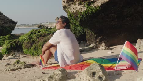 man relaxing on beach with pride flag