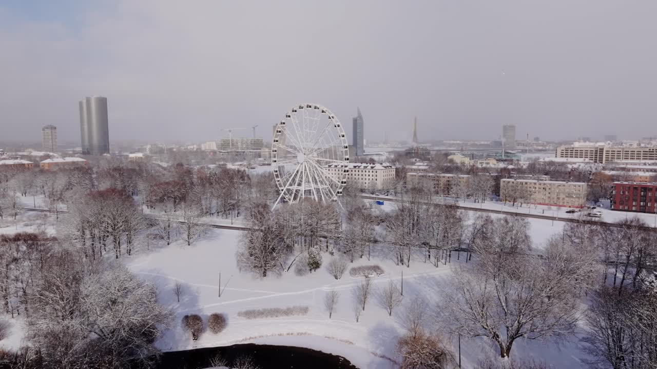 Snow falls gently over Riga city panorama with Ferris wheel, skyline in winter
