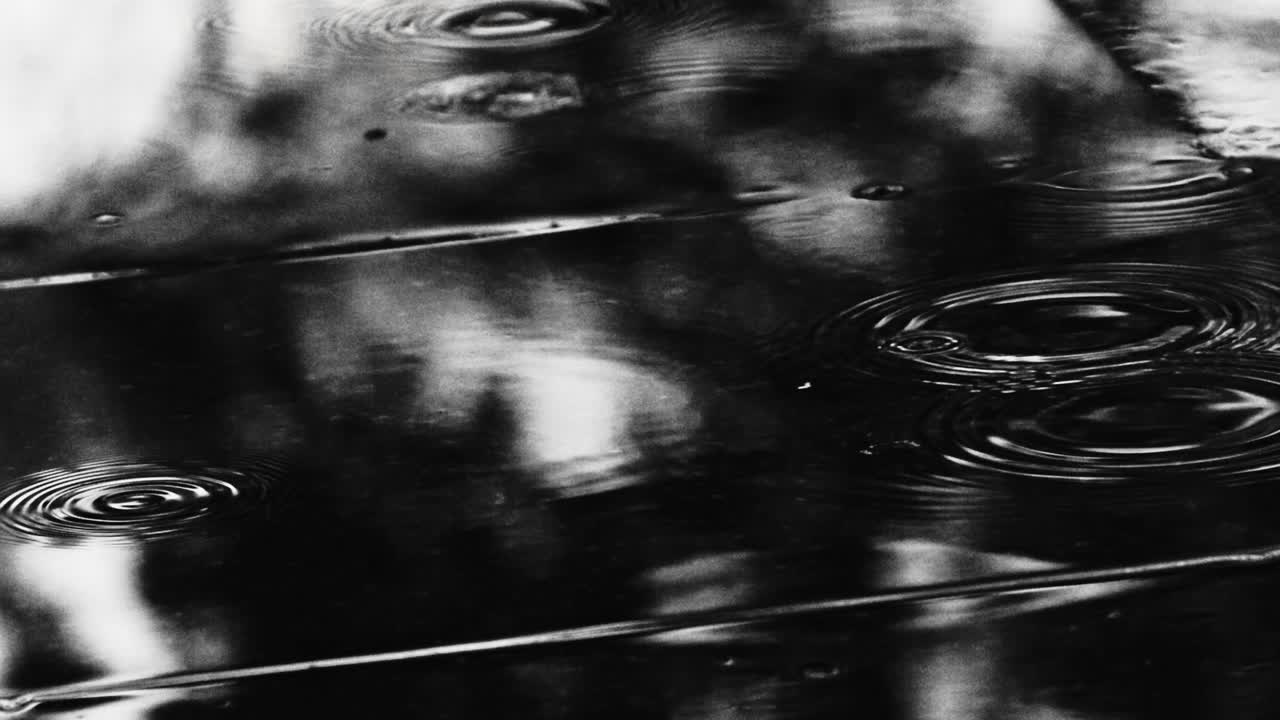 Raindrops falling on a footpath in a shiny rain puddle - close up