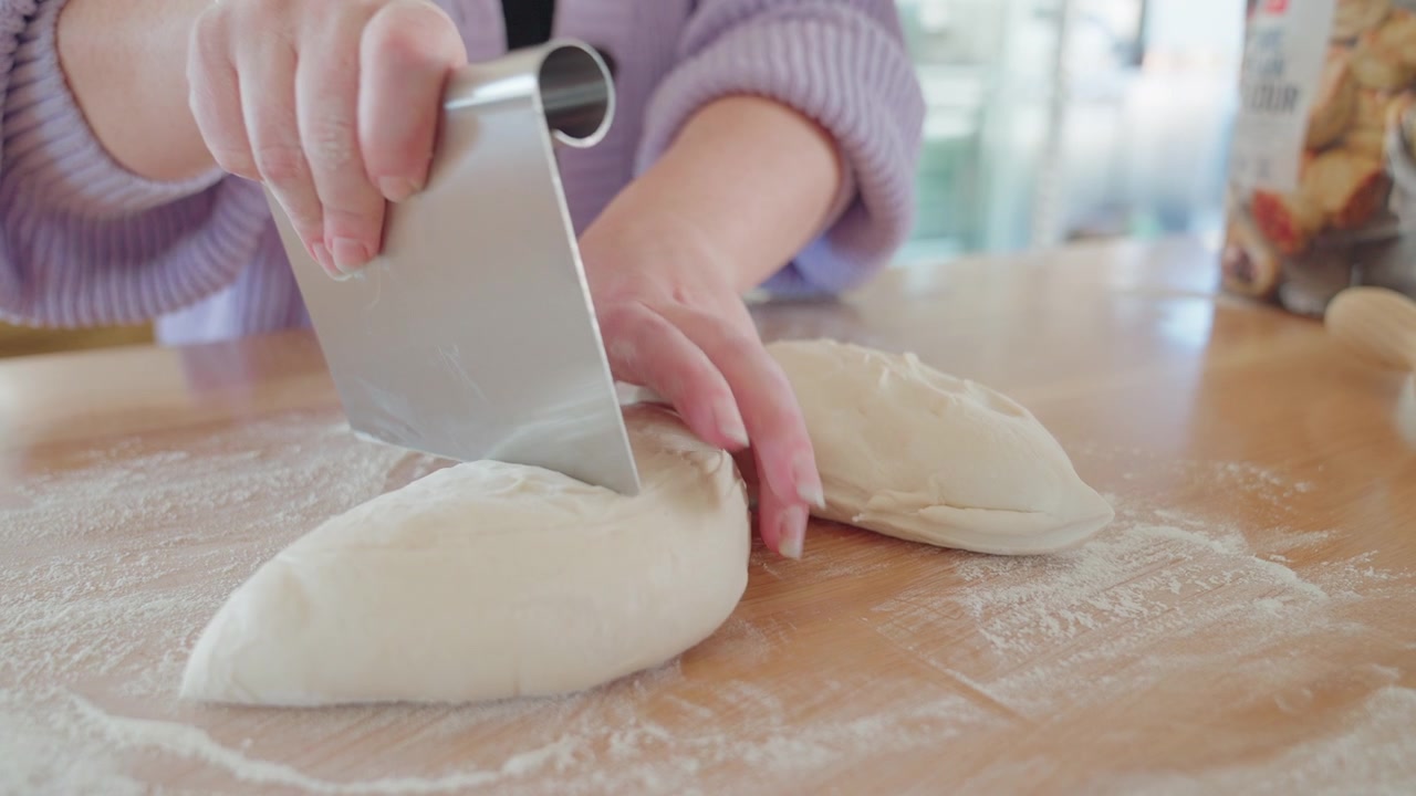 Dough ball being cut in a bright and open kitchen. Pizza and bread on top of counter top and flour