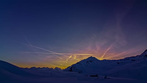 time lapse shot of colorful sky after sunset behind snowy mountains and clear blue sky with flying airplanes